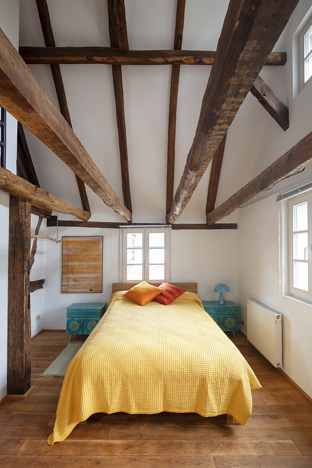 Schlafzimmer mit gelber Tagesdecke unter Fachwerkbalken